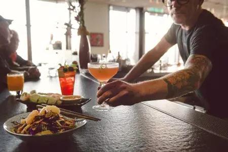 在贝博体彩app的一家酒吧里，酒保正在给顾客递鸡尾酒.